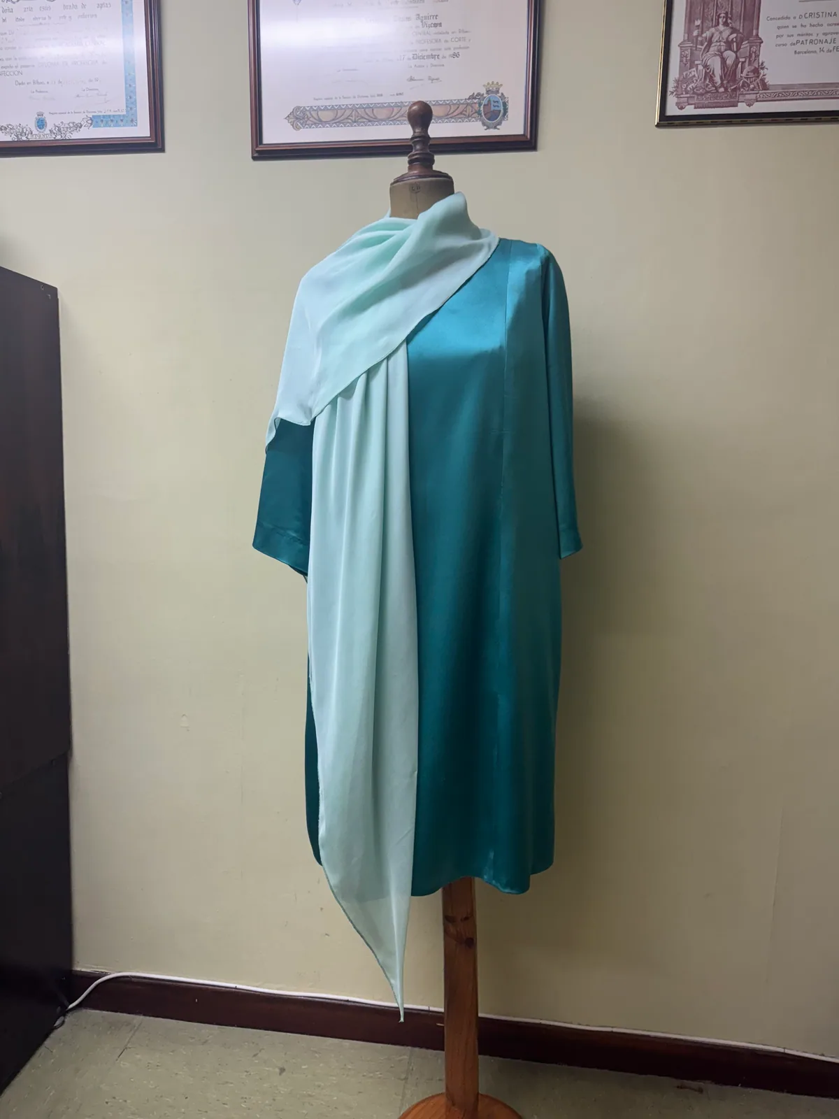Vestido Jade verde azulado sobre maniquí, con una pieza clara cruzada sobre los hombros